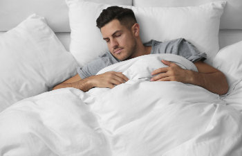 man in gray pajamas sleeps in white sheets