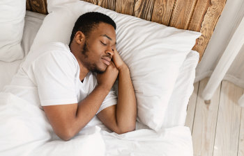 man in white pajamas sleeps in white sheets